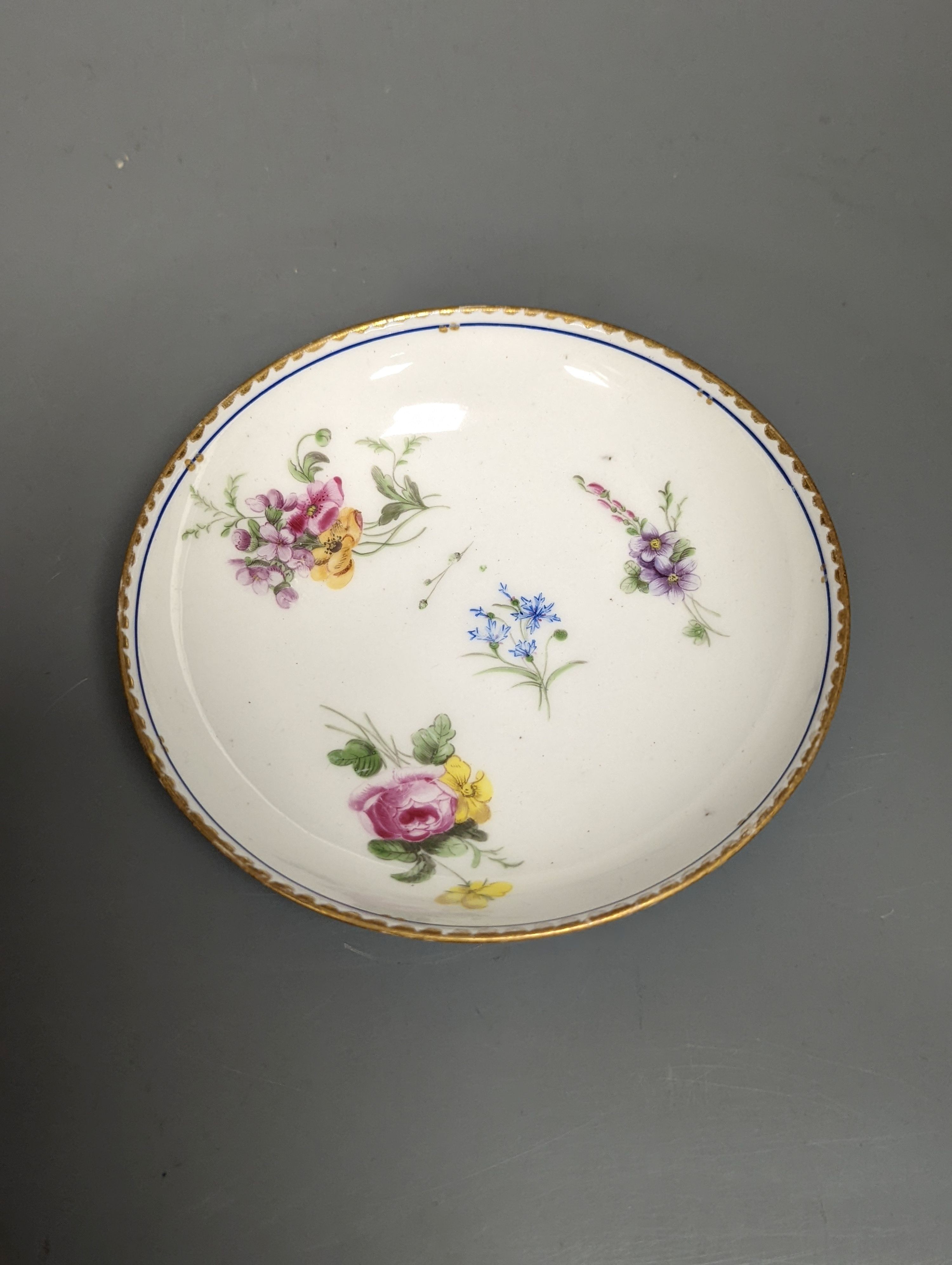 A Sevres coffee cup and saucer painted with floral bouquets under a dentil gilt and blue line border, date code 